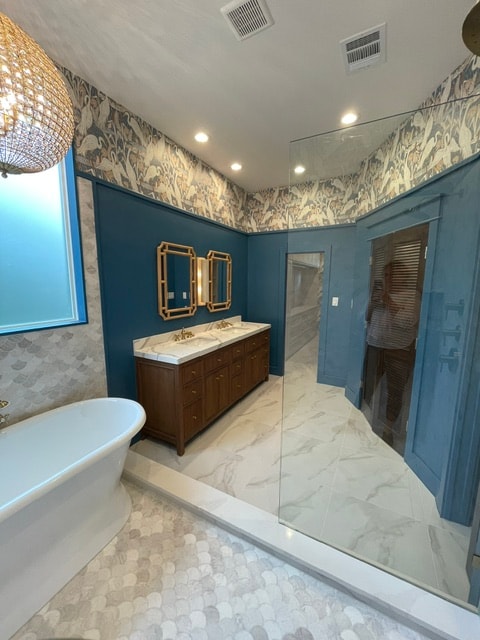 Elegant blue bathroom with patterned wallpaper, a freestanding tub, double vanity, and marble flooring.