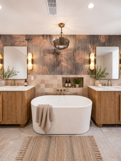 Warm contemporary bathroom with a freestanding tub, wood vanities, patterned wallpaper, and brass fixtures.