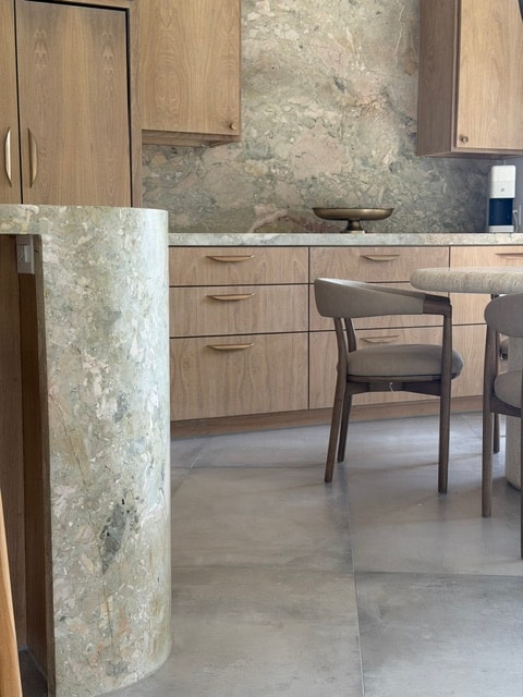 Warm contemporary kitchen with wood cabinetry, stone surfaces, and dining seating.